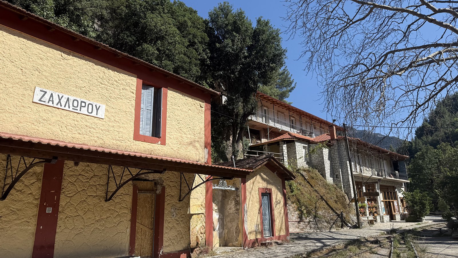 Ο σταθμός της Ζαχλωρούς: η εμαγιέ πινακίδα «ΖΑΧΛΩΡΟΥ» στον κίτρινο σταθμό και οι ράγες του Οδοντωτού που φεύγουν προς το Ρομάντζο.